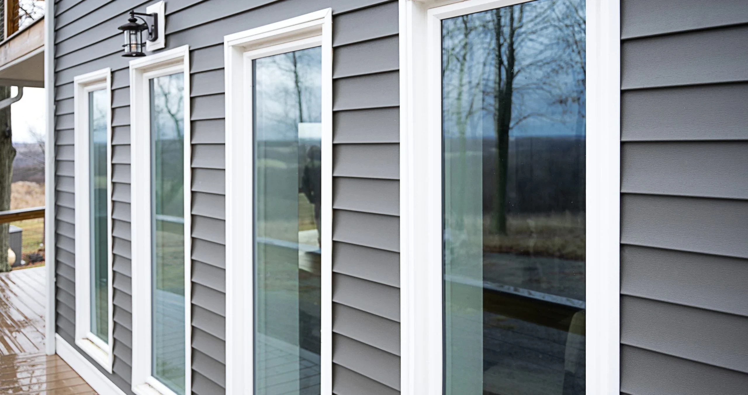 A single-story King William, Virginia home with newly installed exterior siding and replacement windows, showing clean trim lines and a sealed window frame against a wooded rural lot background. The finished exterior shows no gaps between the siding panels and window surrounds.